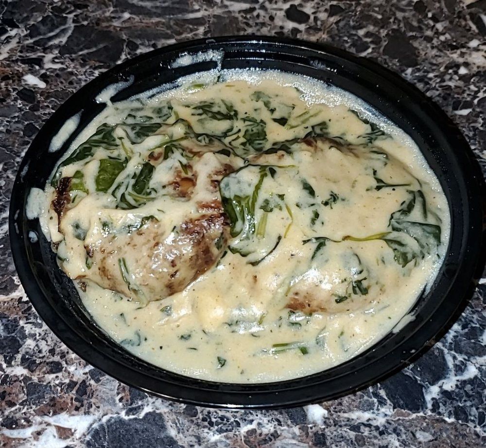 Chicken breasts in creamy spinach sauce in a black bowl.