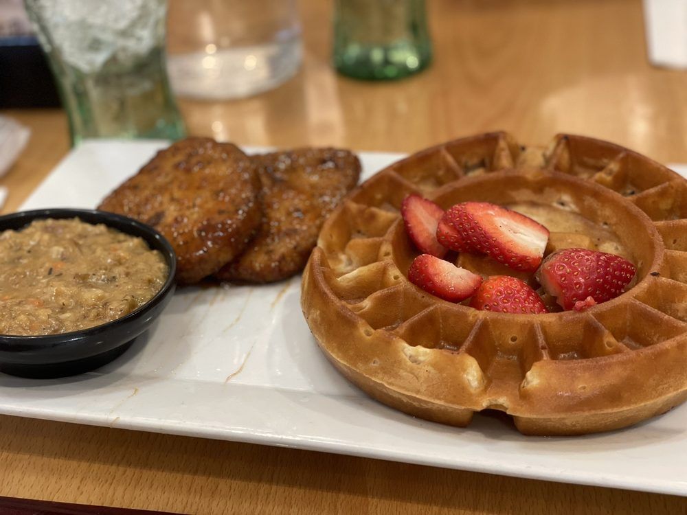 Waffle with strawberries, sausage patties, and gravy on a white plate at a restaurant.
