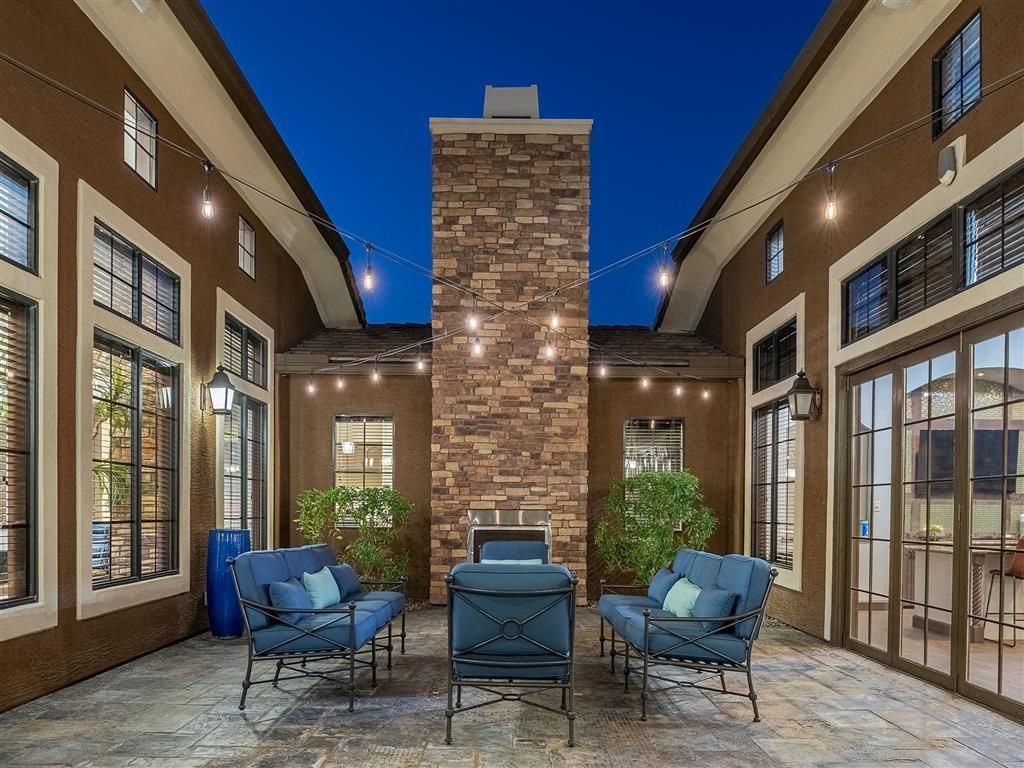 Open-air patio with blue chairs, brick fireplace, and sliding glass doors at dusk