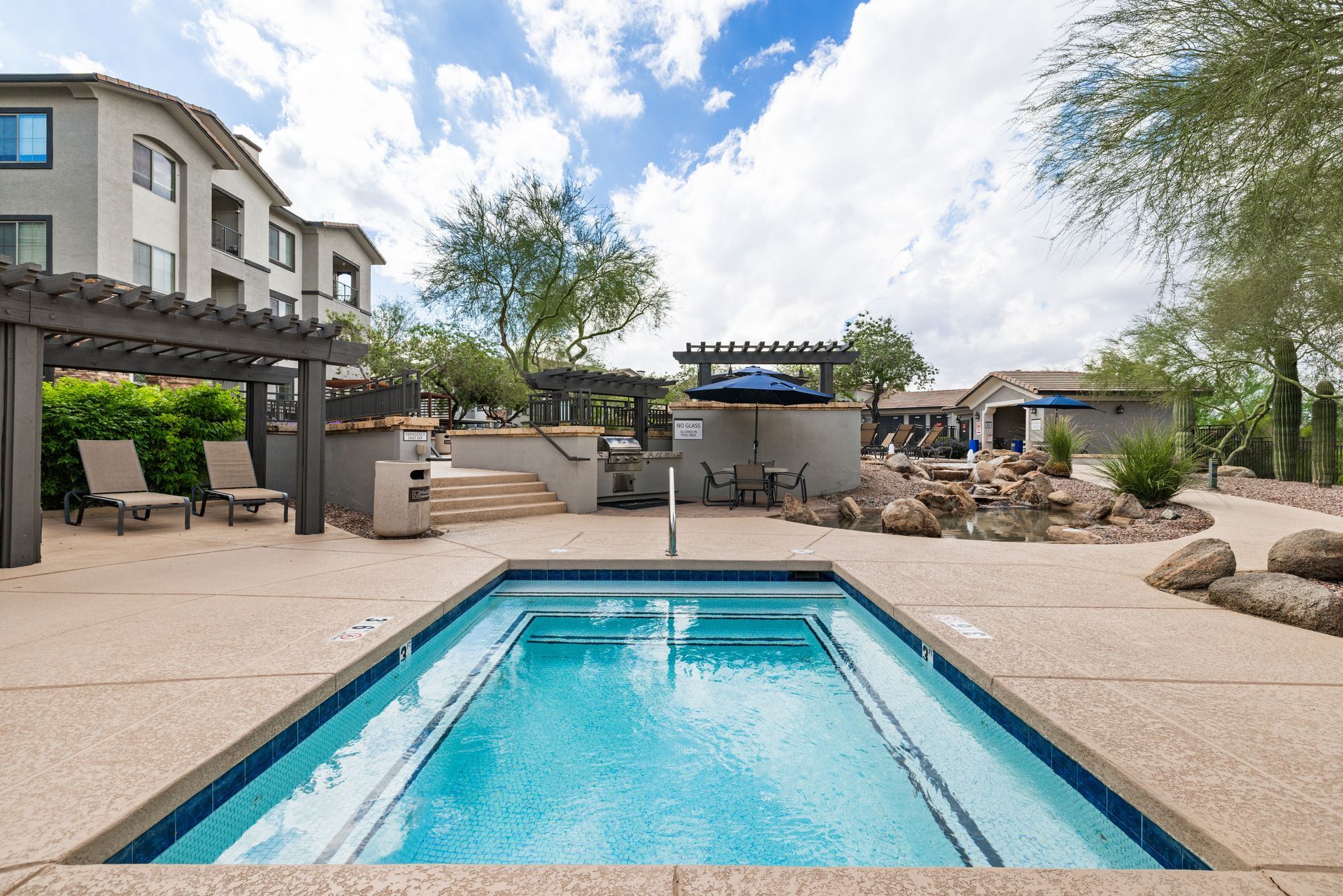 Backyard patio with a swimming pool, lounge chairs, pergola seating, and desert landscaping