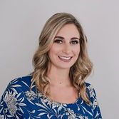 Blonde woman smiling, wearing a blue floral shirt, against a white backdrop.
