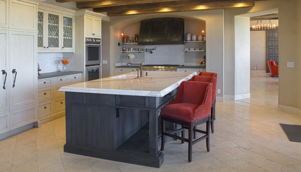 Kitchen with a dark gray island, white cabinets, red bar stools, and a neutral backdrop.