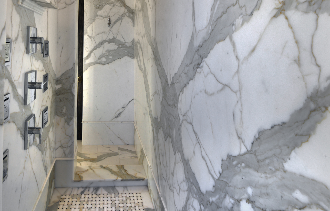 Marble-walled shower with gray veining. Chrome fixtures on left wall.
