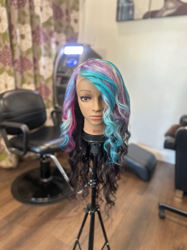 Mannequin head with long wavy teal, pink, and black hair on a stand in a salon chair area