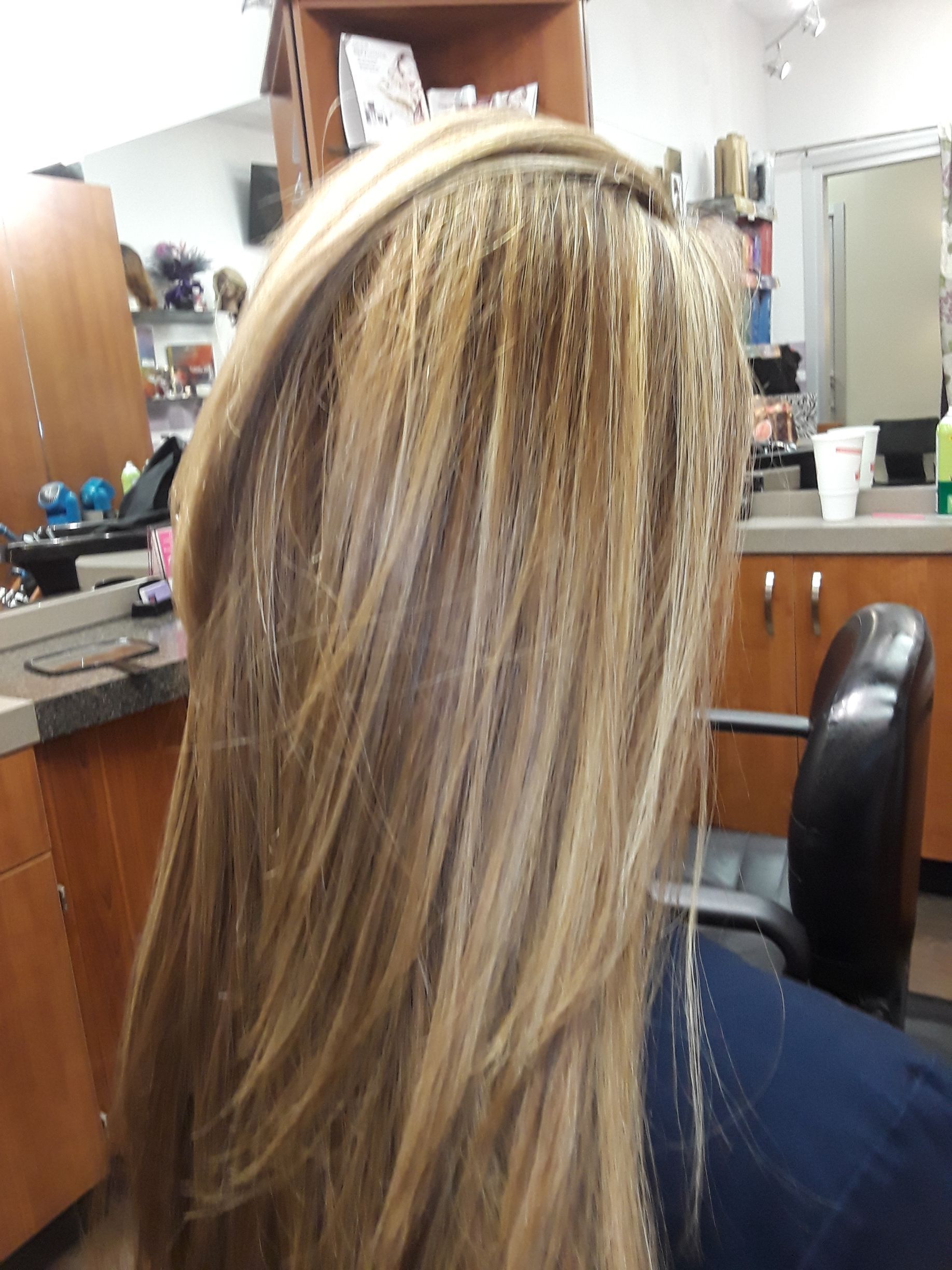 Blonde hair with foiled highlights at a salon station, seen from behind in a mirror-filled workspace