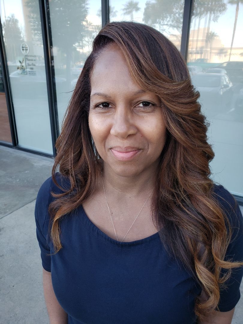 Woman with long wavy hair standing outdoors by a building, wearing a navy top and smiling softly.