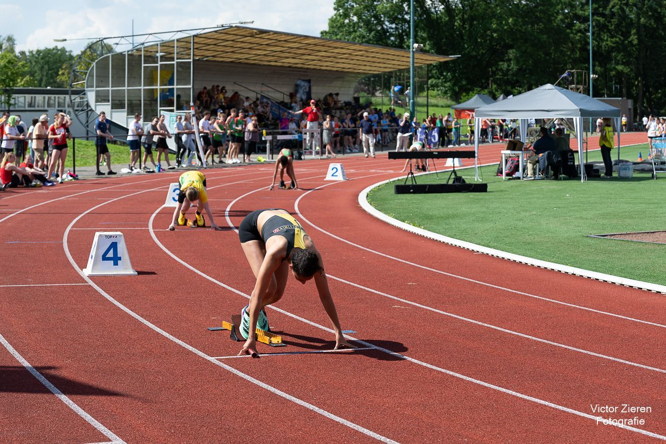 Een sprinter staat aan de start op een rode baan, met op de achtergrond een menigte.