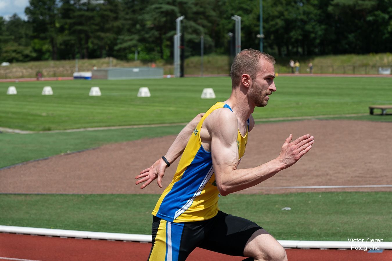 Loper in geel en blauw hemd op de baan.