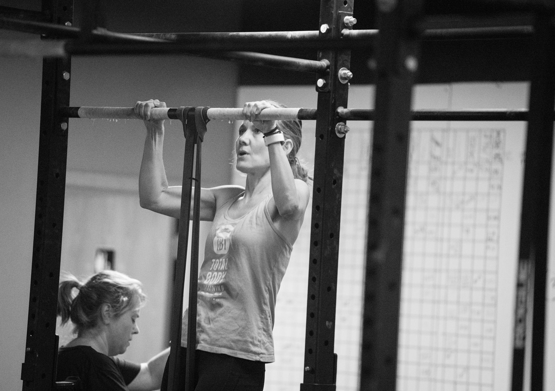 A woman is doing a pull up on a bar in a gym.