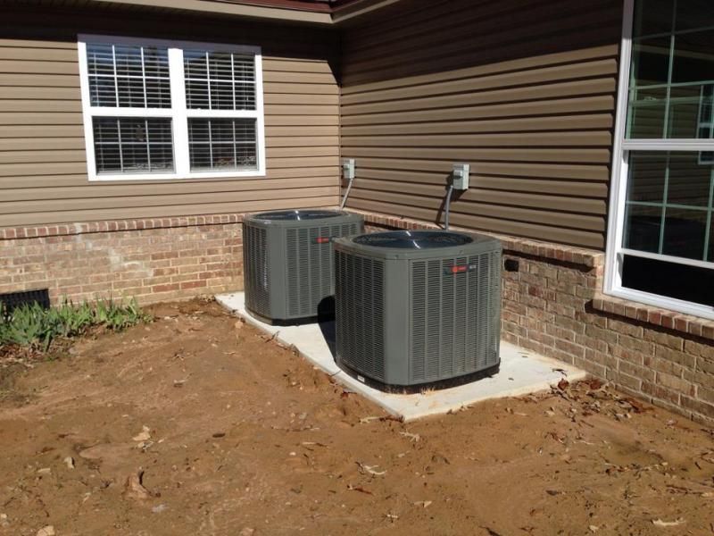 Two gray HVAC units on a concrete pad next to a brick and brown siding house.