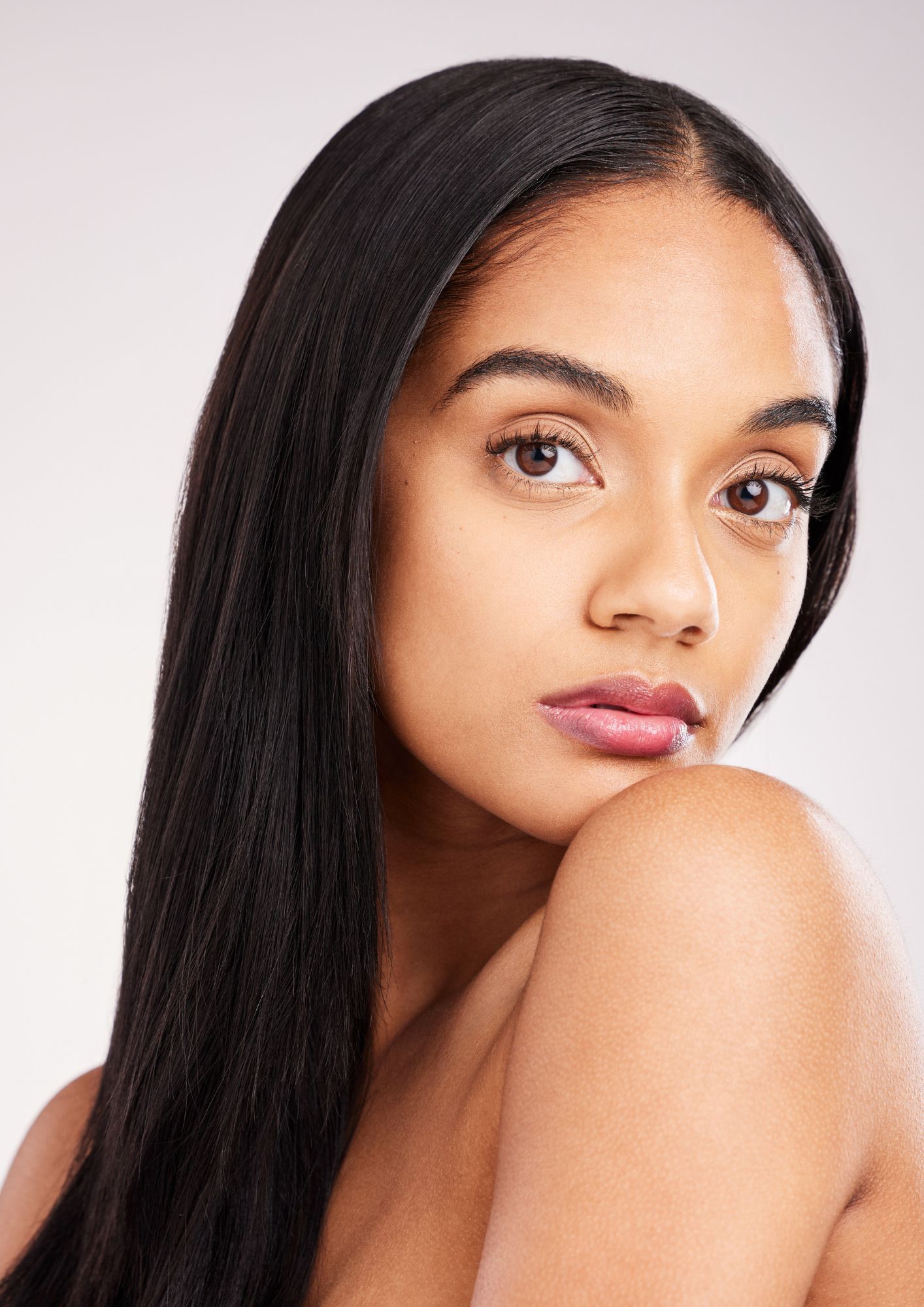 A woman with long black hair is looking at the camera with her hand on her shoulder.
