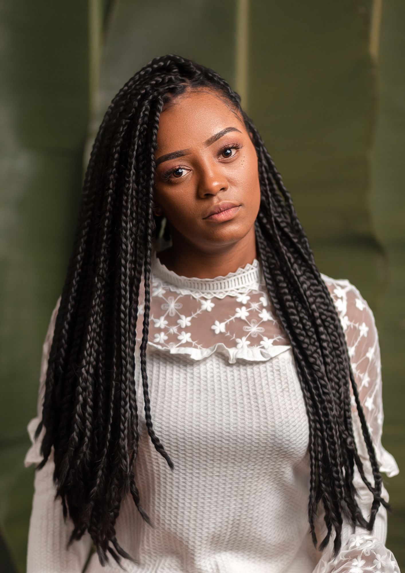 A woman with braids is wearing a white sweater and looking at the camera.