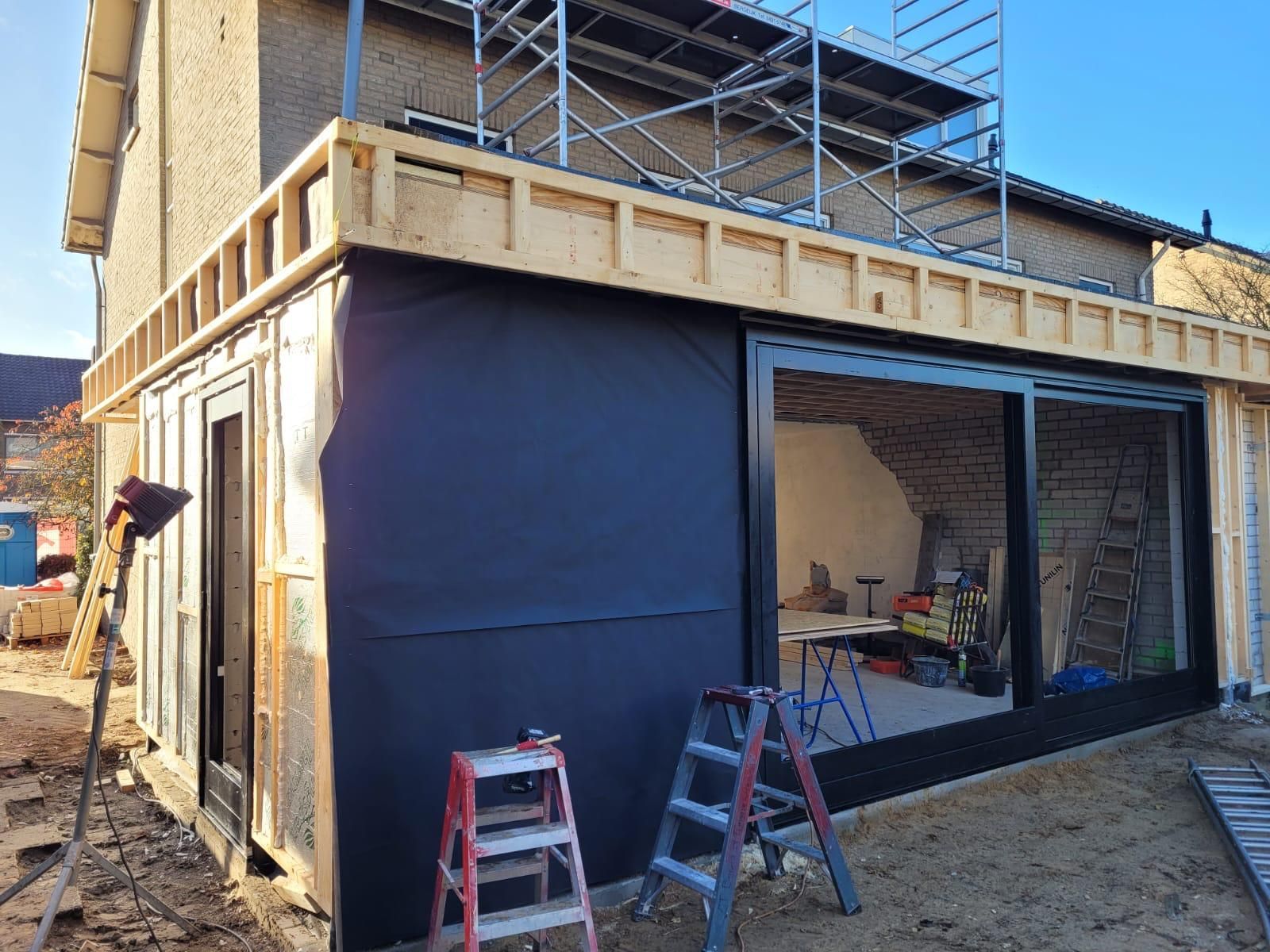 Er wordt een huis gebouwd met steigers en een groot raam.