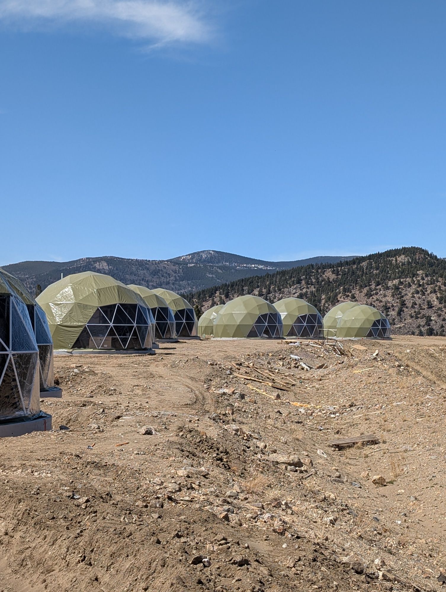 A row of tents sitting on top of a dirt field with mountains in the background.