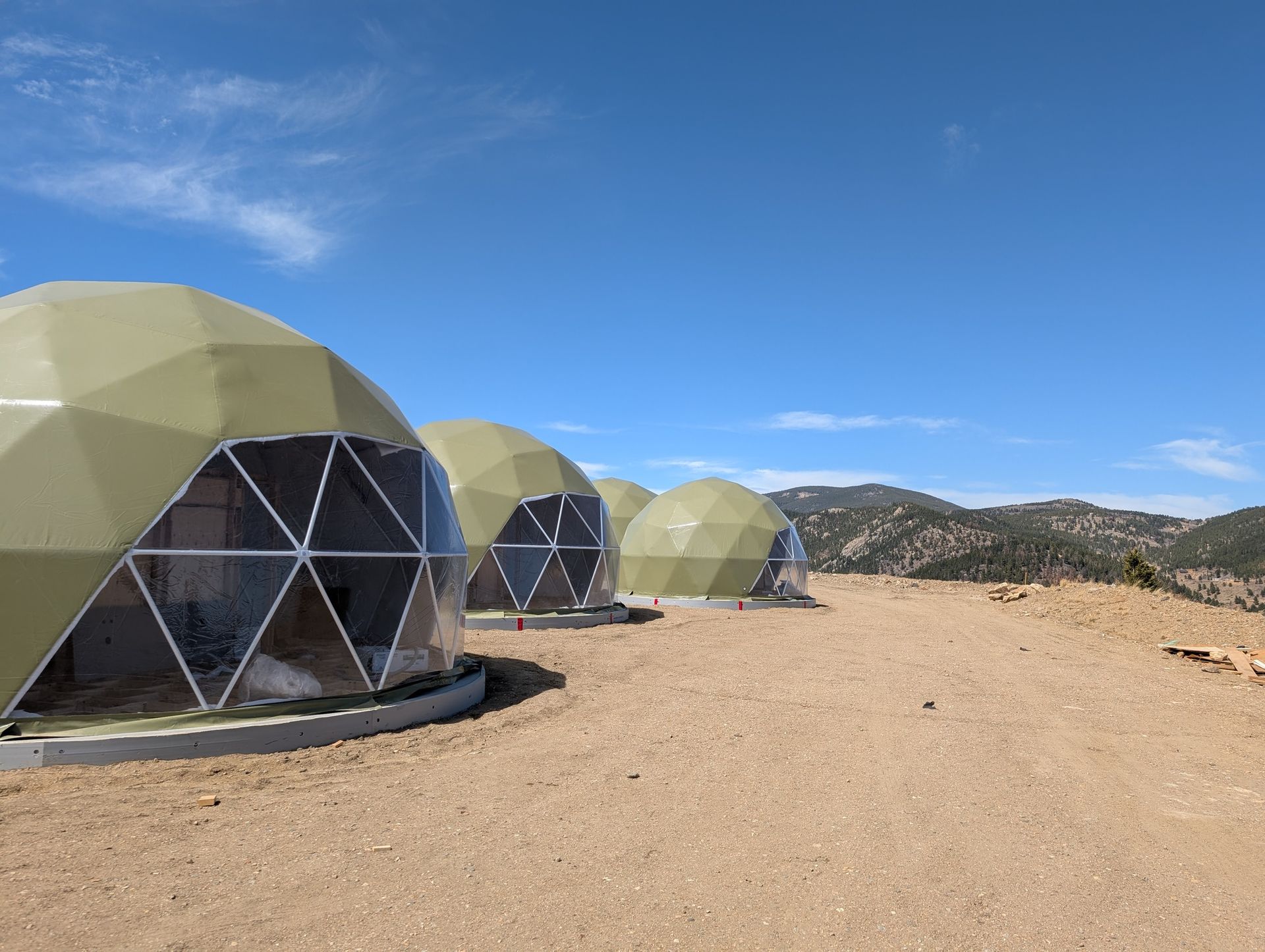 A row of dome tents are sitting on top of a dirt field.