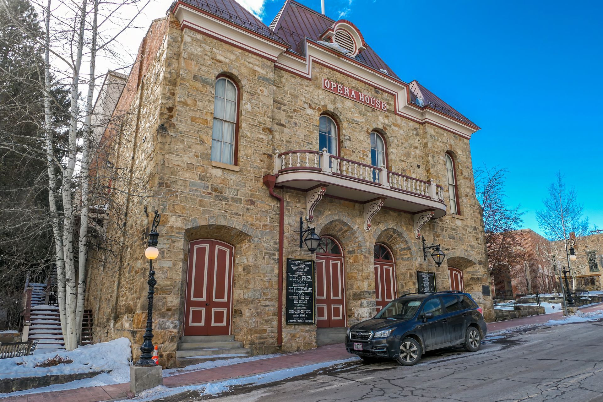 Historic stone building with red doors and balcony, car parked on street.