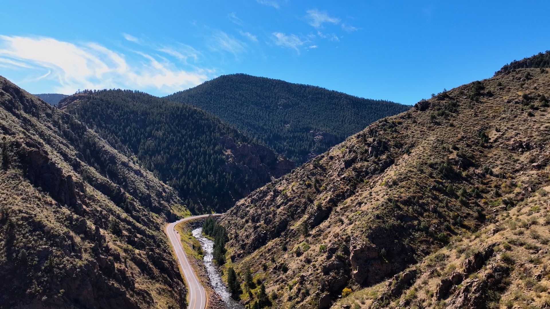 A mountain pass with a river and road winding through it under a blue sky.
