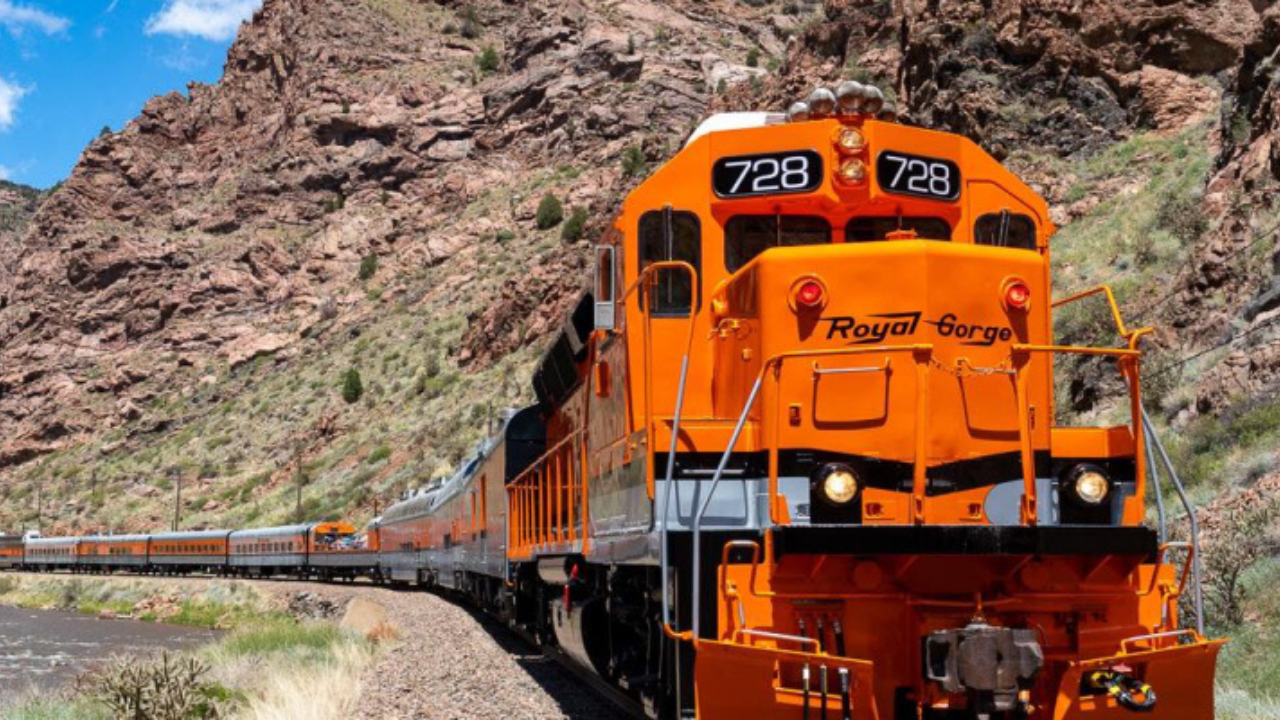 A train is going down the tracks next to a mountain.