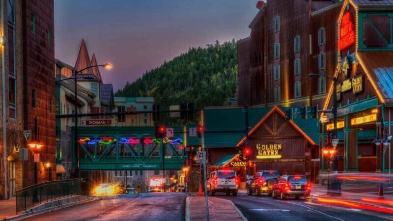 A city street with a bridge over it and cars driving down it at night.