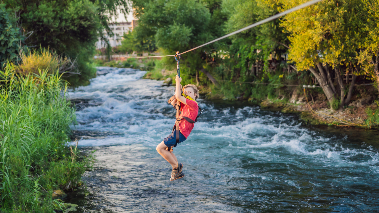 A young boy is riding a zip line over a river.