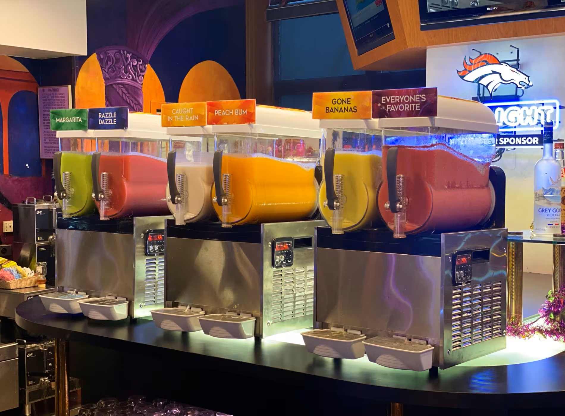 A row of slushy machines are lined up on a bar.
