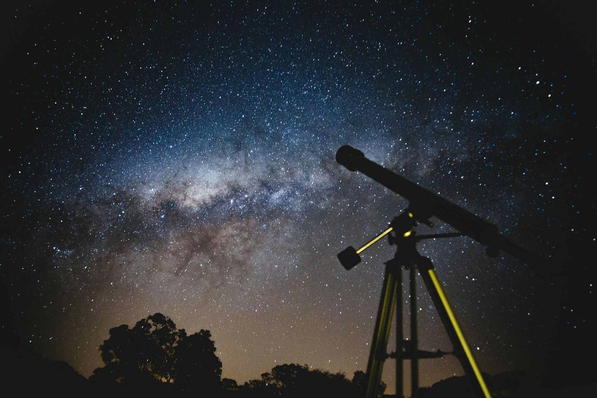 A telescope is sitting on a tripod under a starry night sky