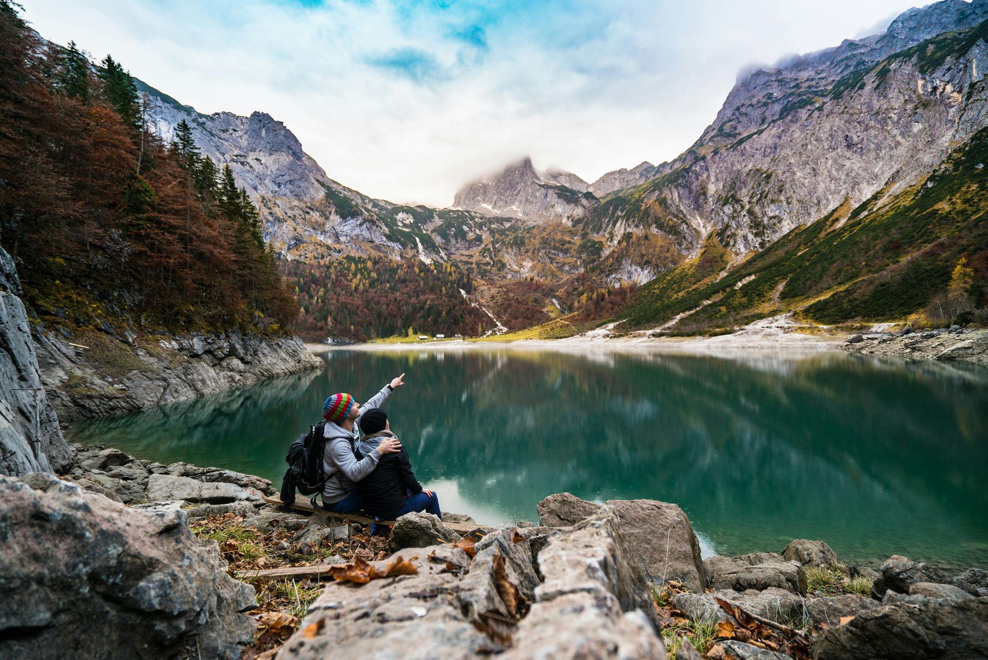 A couple is sitting on a rock near a lake in the mountains.