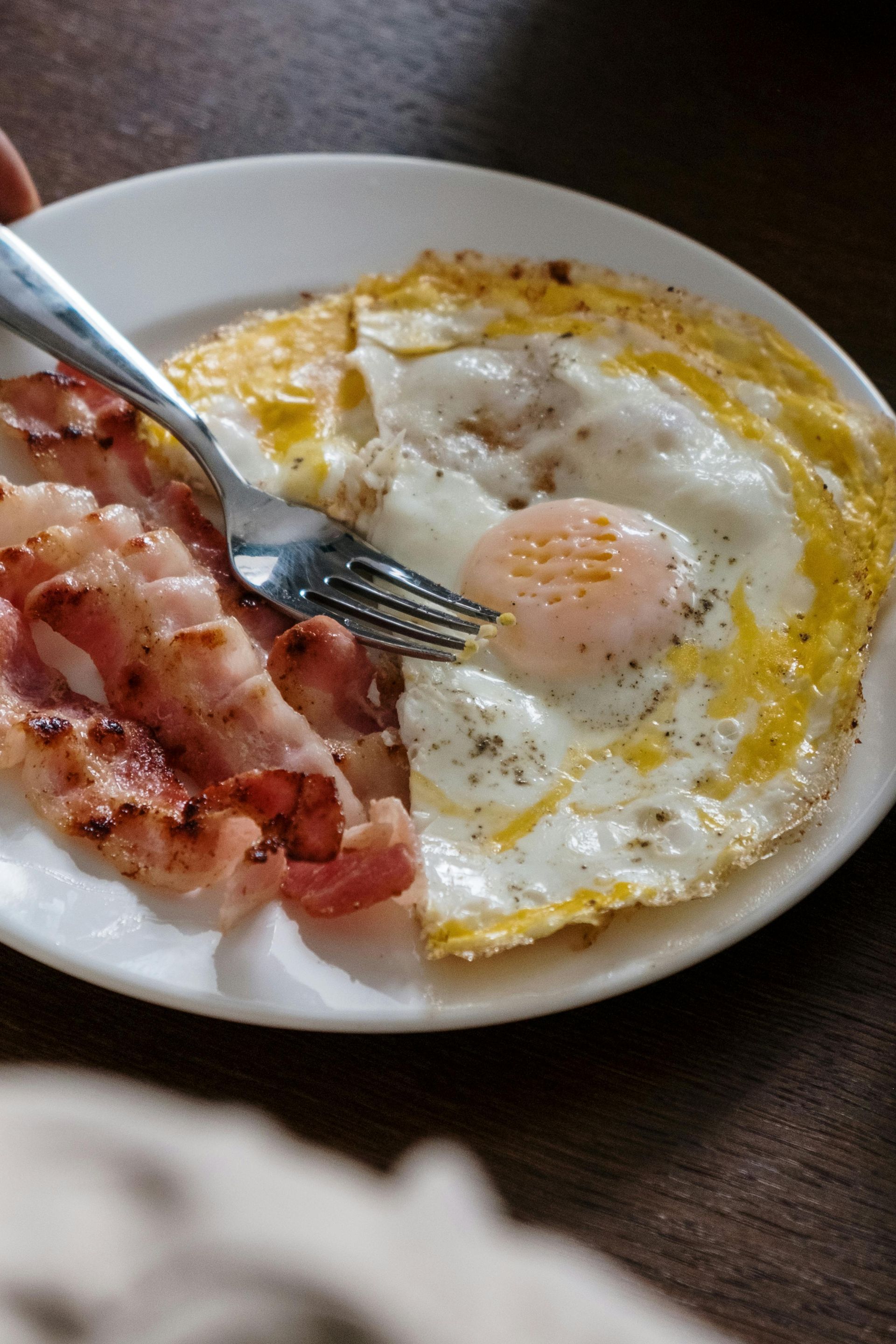 A person is eating a plate of bacon and eggs with a fork.