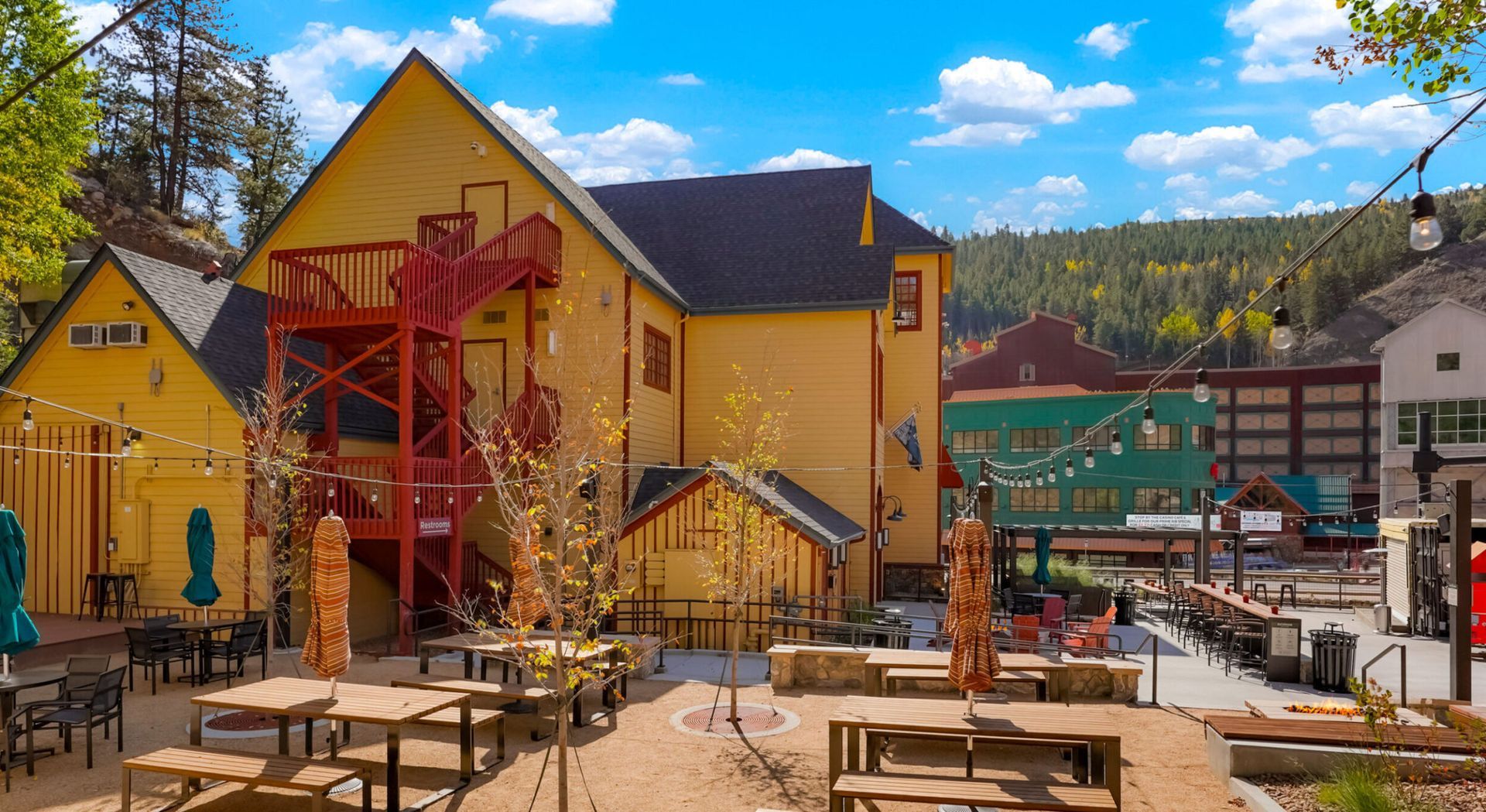 A large yellow building with a red fire escape and tables and chairs in front of it.