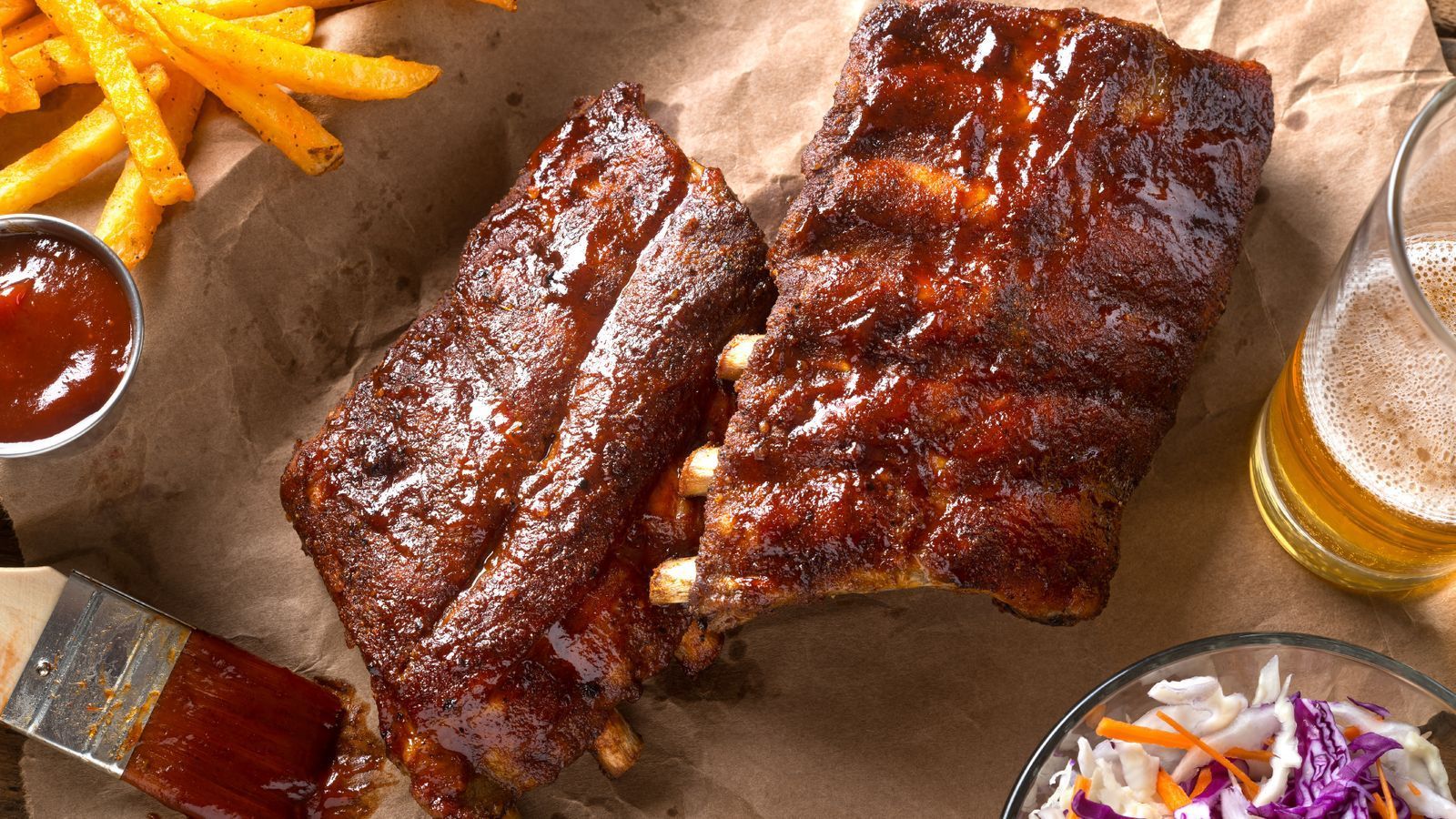Ribs , french fries , coleslaw and a glass of beer on a table.
