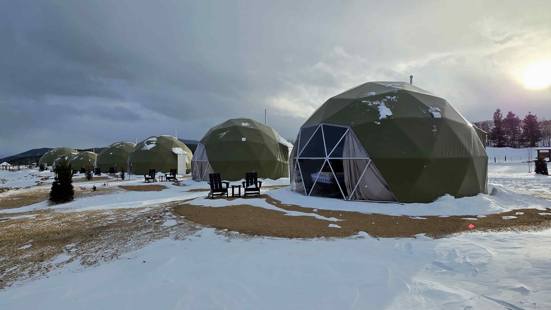 A group of tents are sitting on top of a hill surrounded by trees.