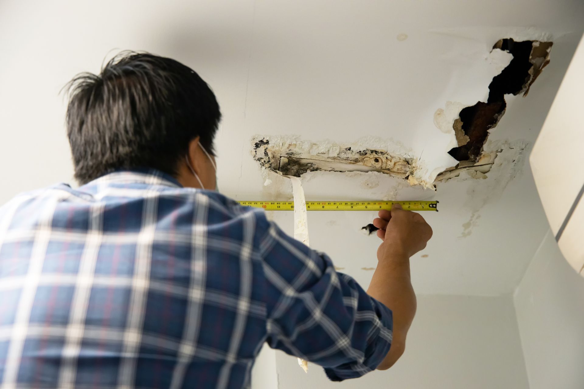 Skilled worker repairing and fixing ceiling panels damaged by water leakage from pipes, ensuring a seamless restoration process for water damage repair in the roof house.