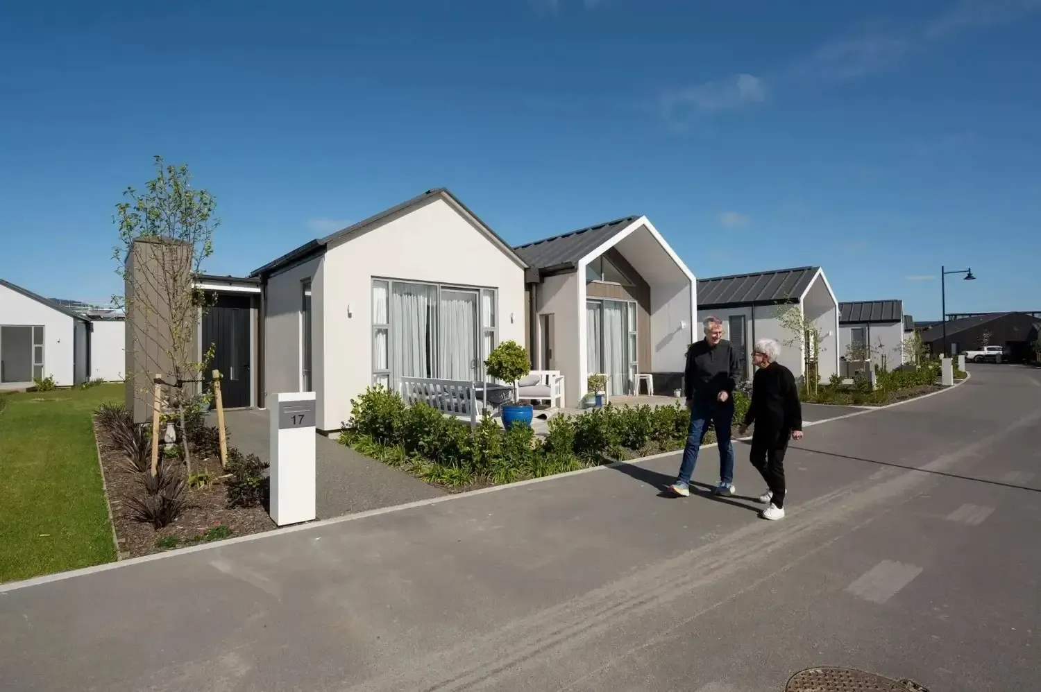 Couple walking on a road in front of modern bungalows on a sunny day.