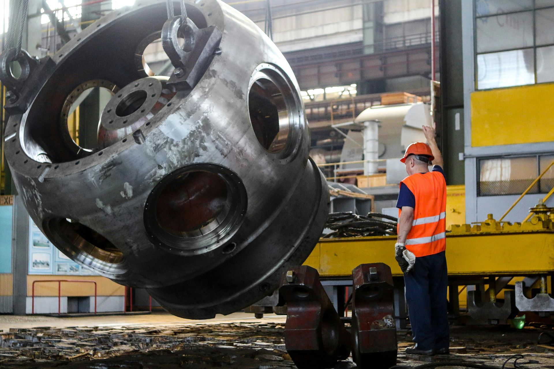 A man is standing next to a large metal object in a factory.