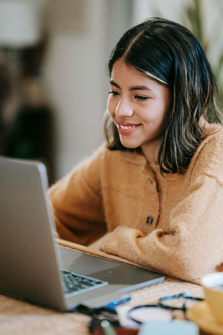 A young woman is sitting at a table using a laptop computer.