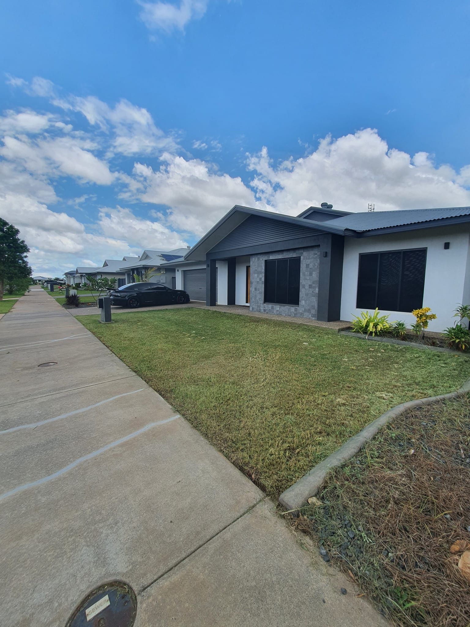 Gas station with brown gravel landscaping, tree, and cloudy sky. A train crossing is visible — Green Scene NT in Darwin, NT