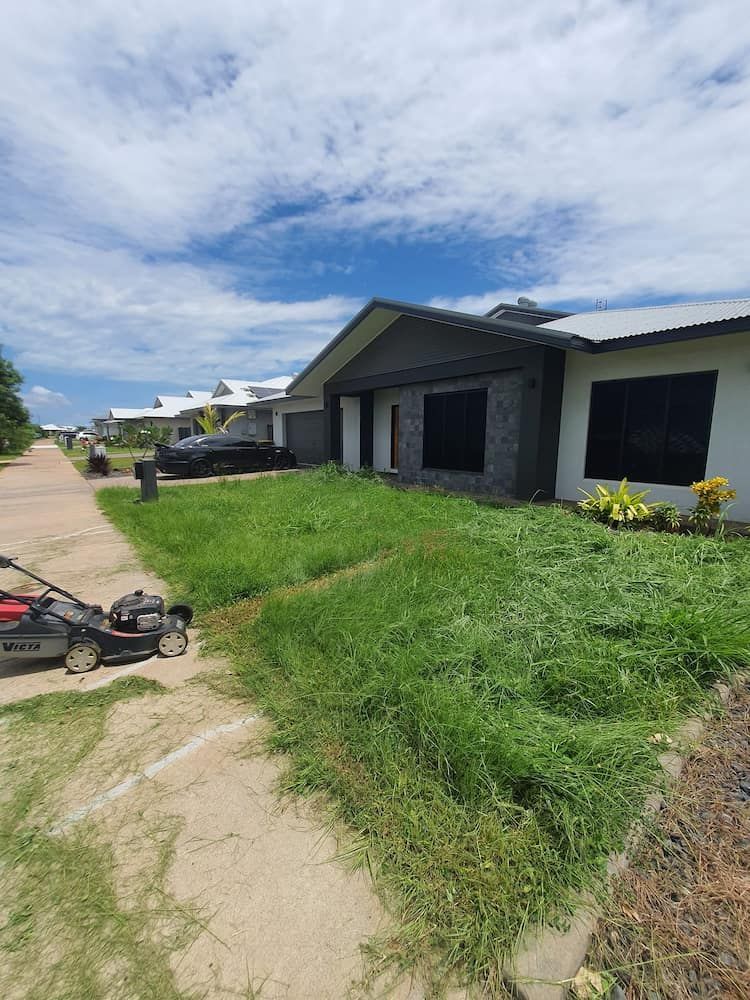 A lawn mower cutting overgrown grass in front of a house on a sunny day — Green Scene NT in Darwin, NT