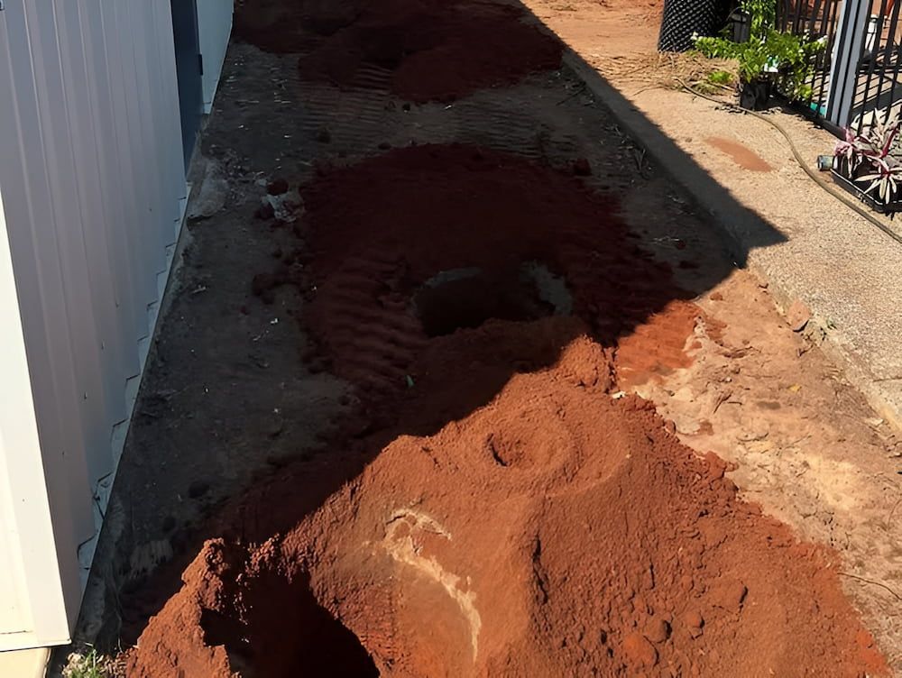 Red Dirt With Holes Dug Along a White Building and Sidewalk — Green Scene NT in Darwin, NT