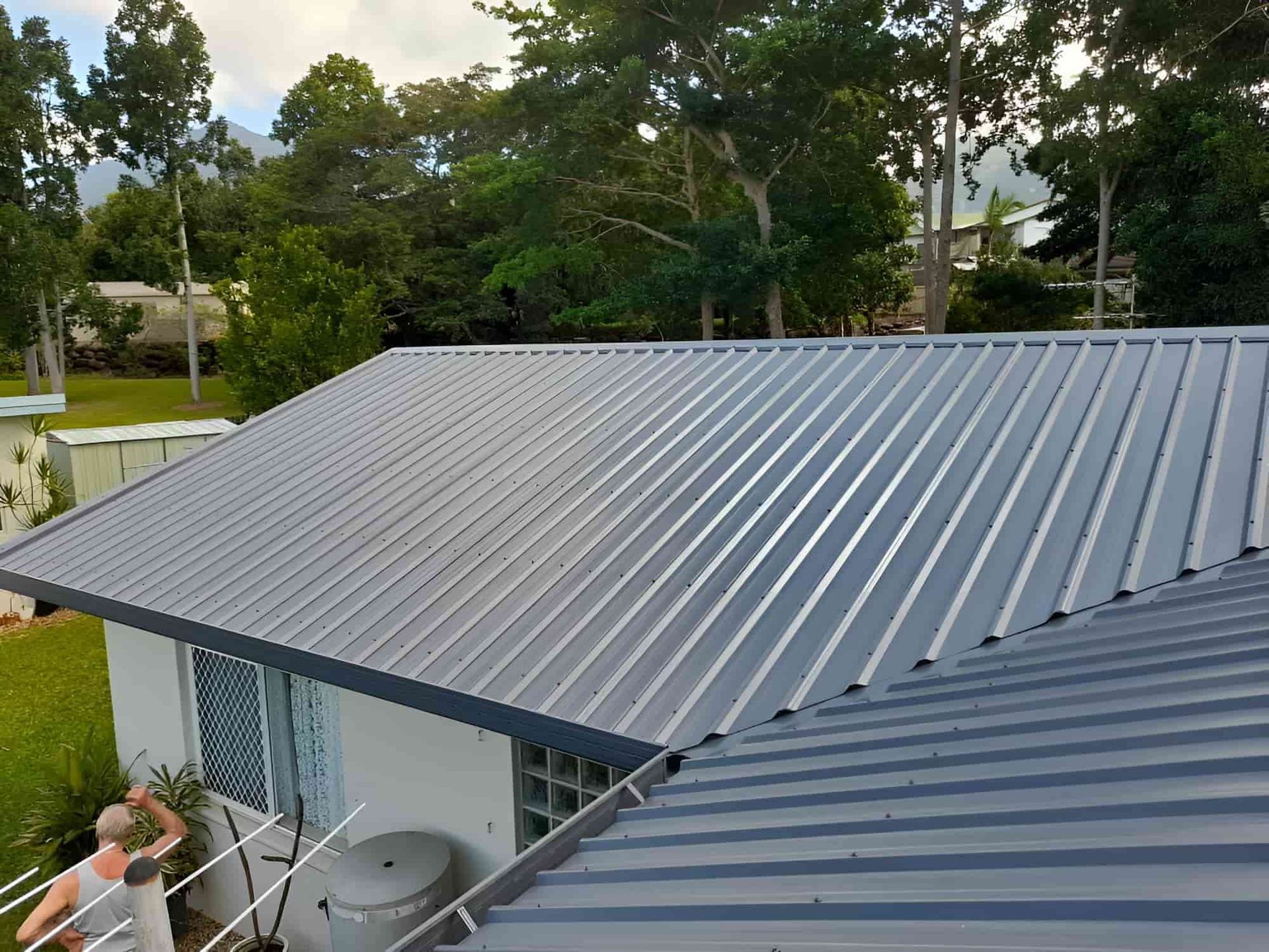 A Man Is Standing On The Roof Of A House — Kiwi Painter In Cairns, QLD