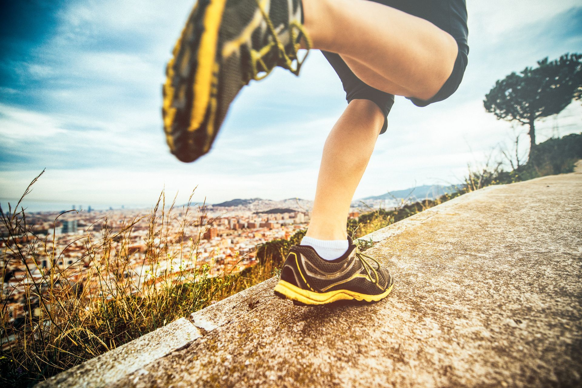 Person running on a path overlooking a city, wearing black and yellow shoes.