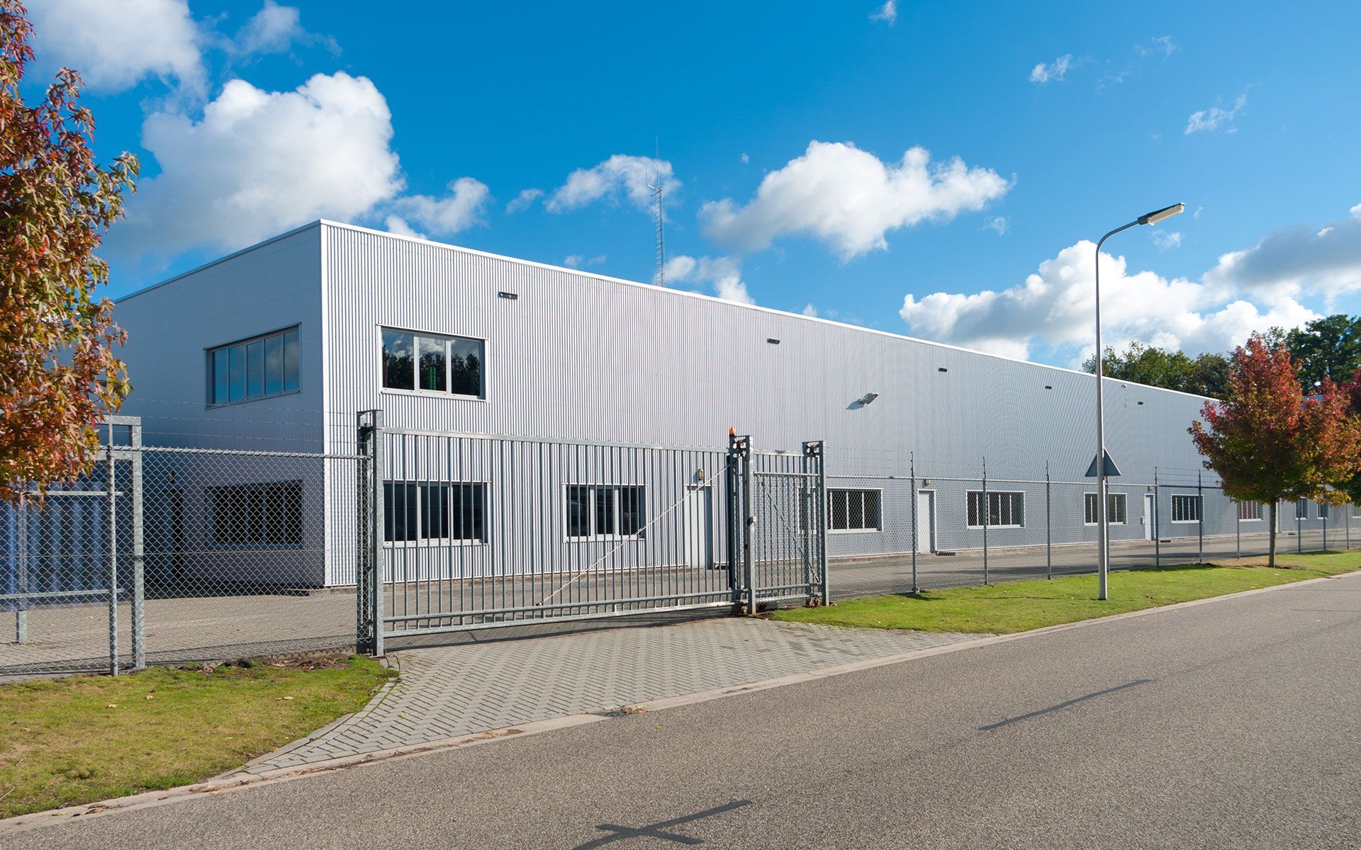 A large white building with a fence around it is sitting next to a road.