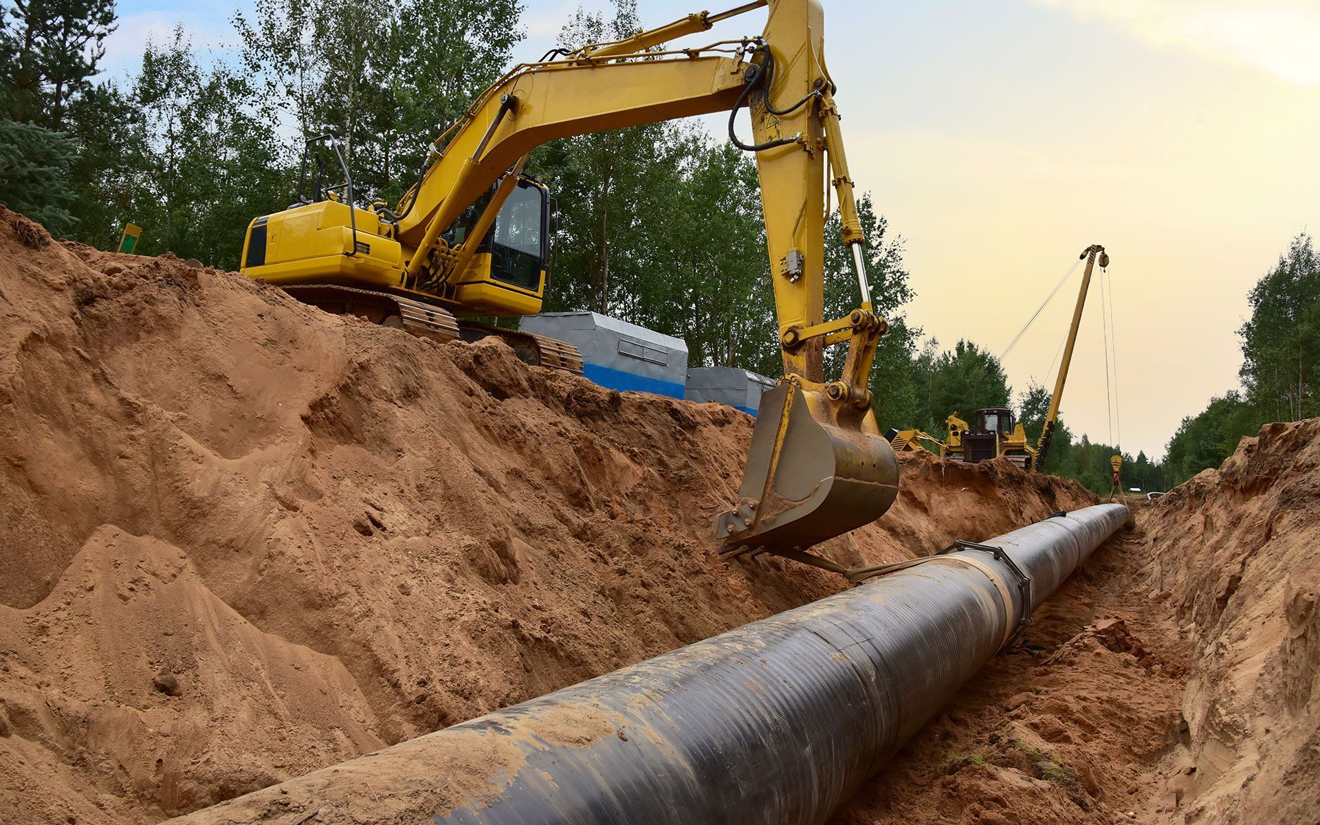 A yellow excavator is digging a hole for a pipe.