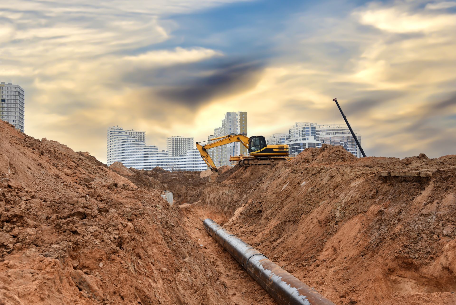 A yellow excavator is digging a trench for a pipe.
