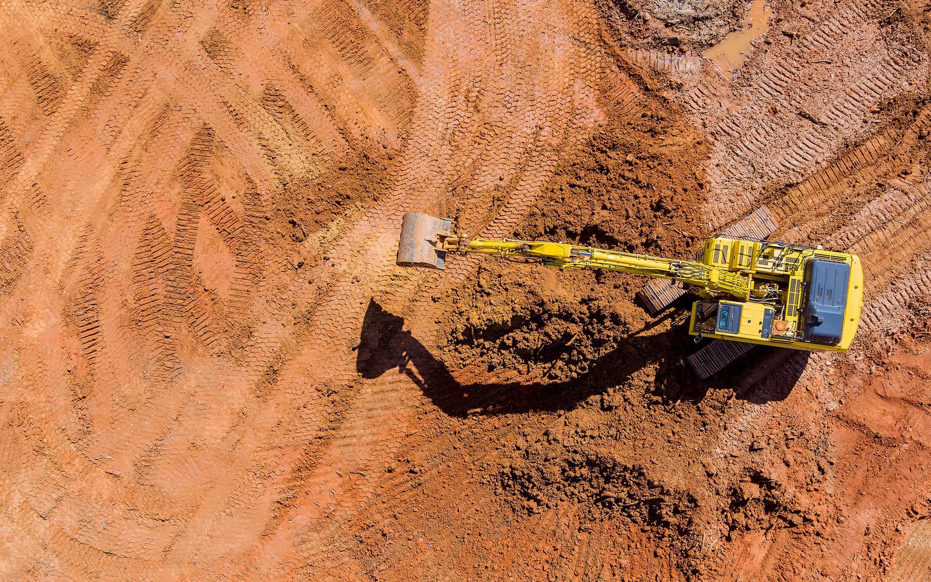 An aerial view of a yellow excavator working on a dirt field.