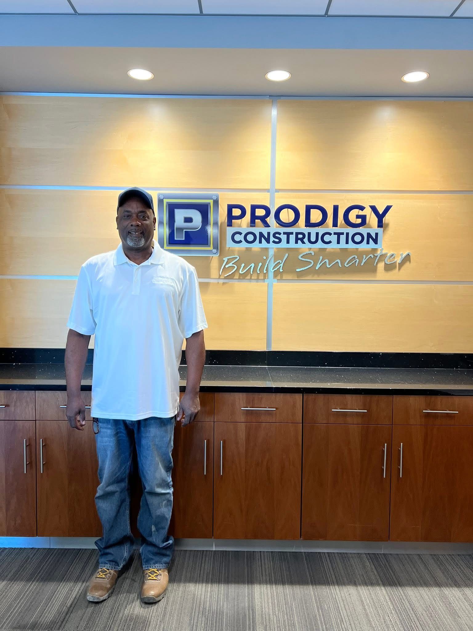 Derwin is standing in front of a sign for Prodigy Construction.