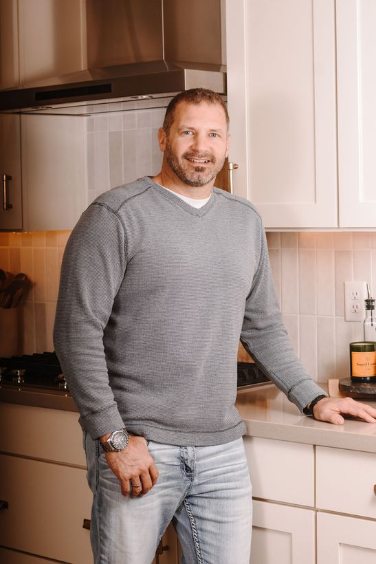 A man in a sweater and jeans is standing in a kitchen.