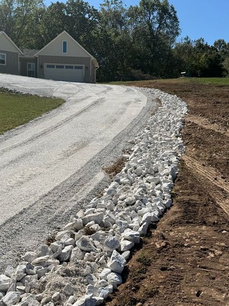Gravel driveway bordered by white rocks, leading to a house with a garage, sunny day.