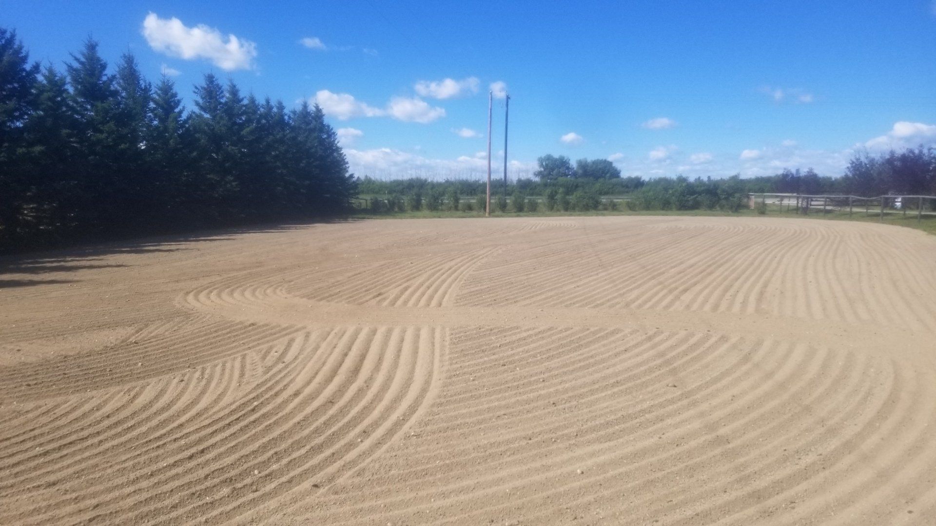 A large dirt field with trees in the background on a sunny day.