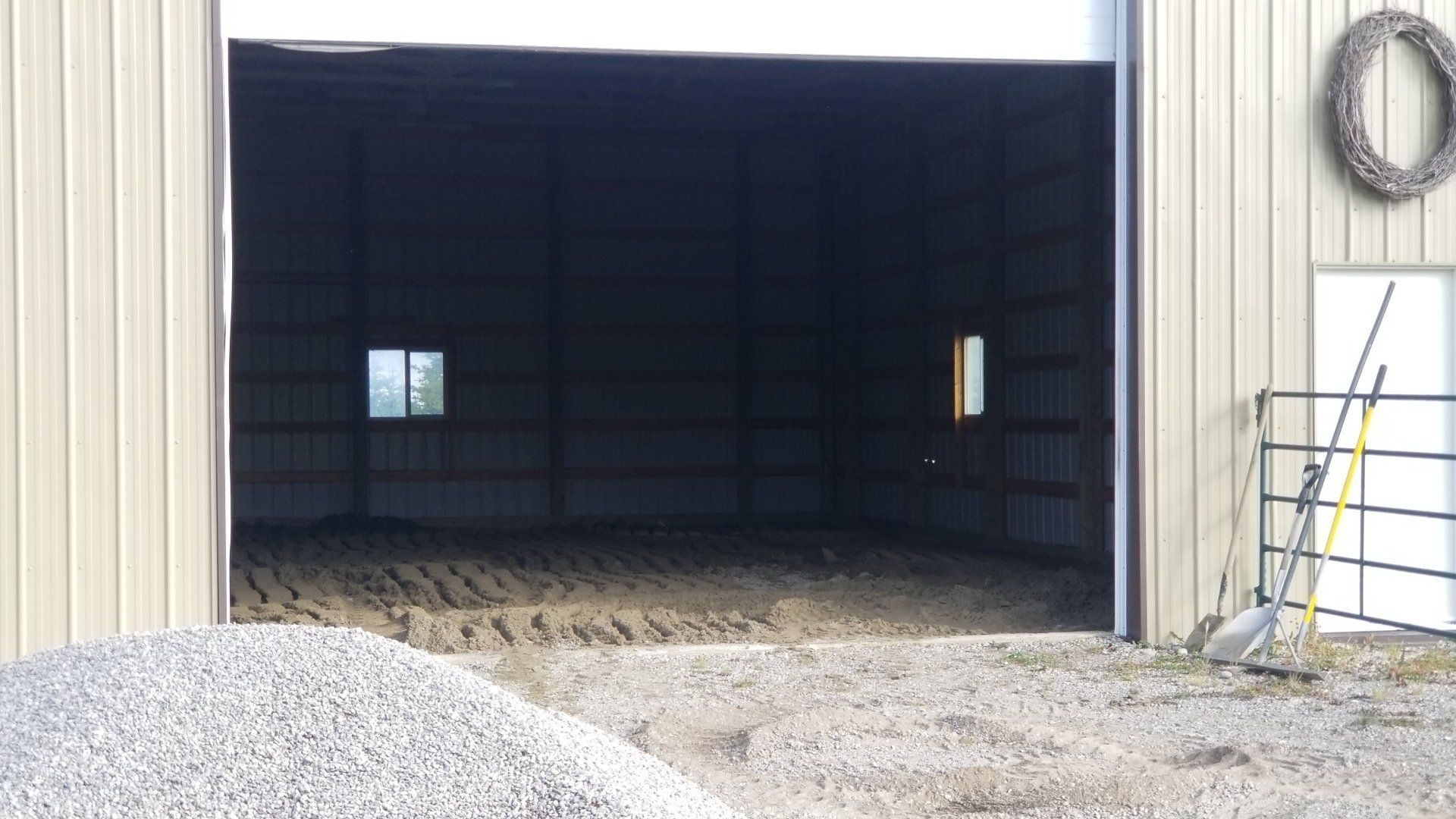 A large empty barn with the door open and a pile of gravel in front of it.