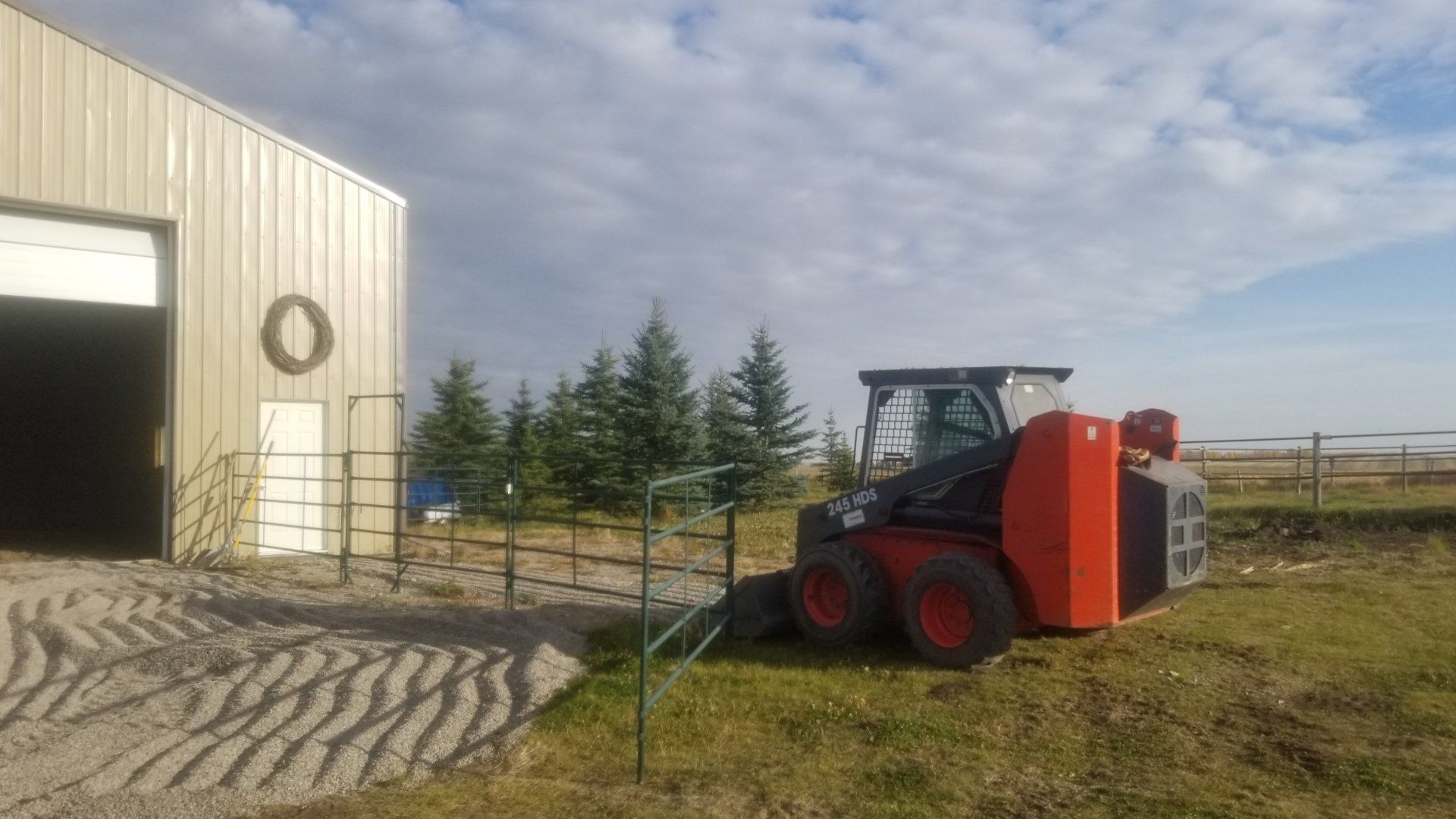 A red and black skid steer is parked in front of a building.